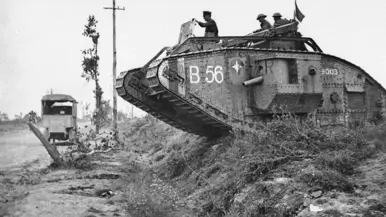 Een zwart-witfoto van een tank met nummer B 56 in een modderig landschap, met soldaten erop en een voertuig op de achtergrond.