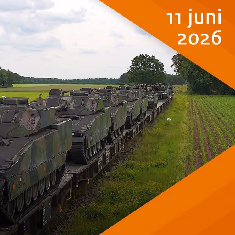 Militaire voertuigen op trein in gras- en boslandschap.