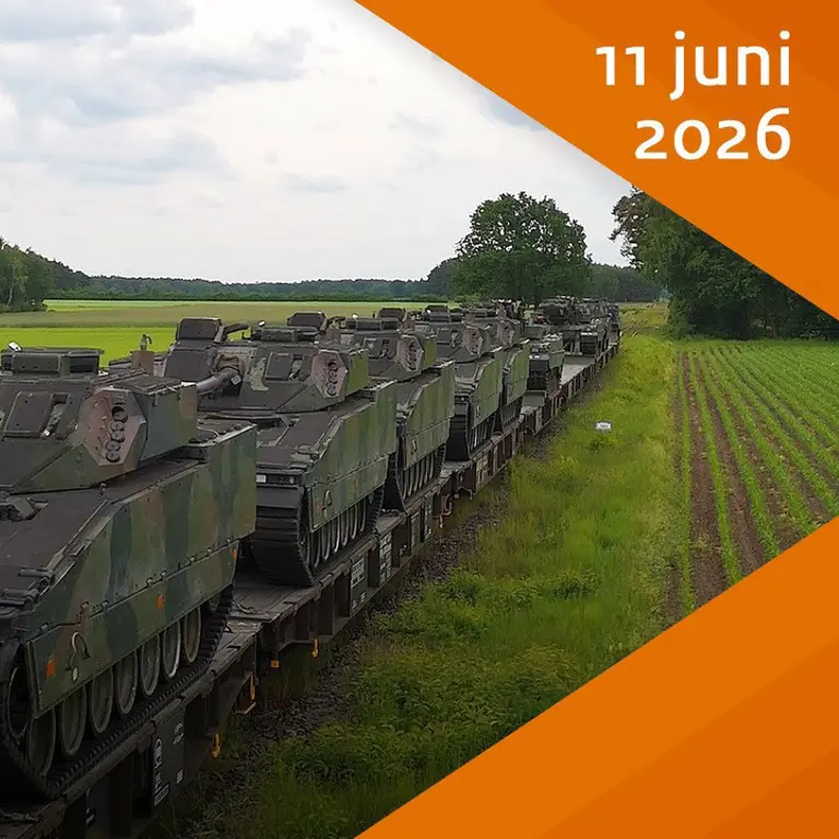 Militaire voertuigen op trein in gras- en boslandschap.