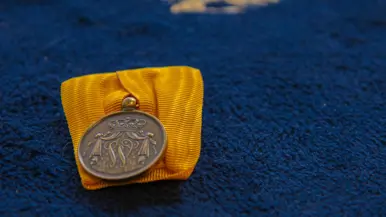Medaille met oranje lint op een koningsblauw tapijt. Boven de medaille op het tapijt staat het luchtmachtembleem met adelaar en kroon in goud gedrukt.