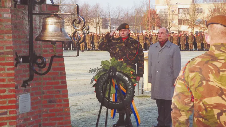 Militair salueert  naar krans en monument tijdens herdenkingsceremonie.