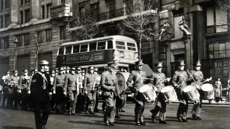 Zwart-witfoto van militair orkest dat speelt op straat met bus op de achtergrond