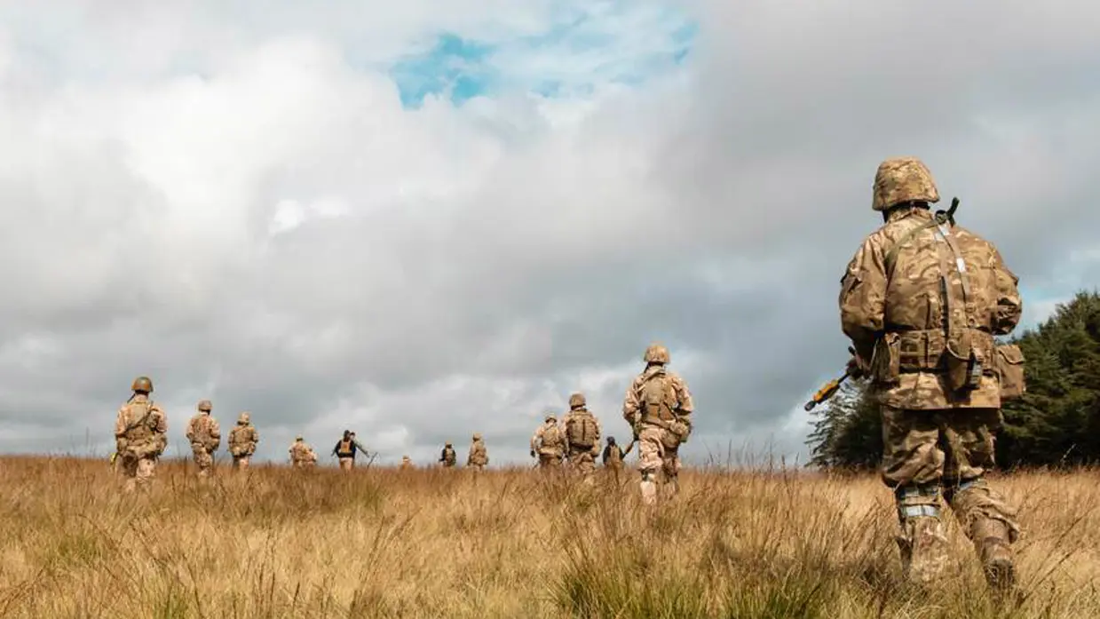 Militairen lopen door graslandschap.