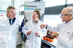 Staatssecretaris Tuinman in witte jas met veiligheidsbril praat bij de Brightlands Chemelot Campus met 2 mannen in witte jassen.