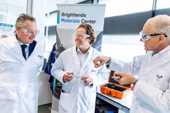 Staatssecretaris Tuinman in witte jas met veiligheidsbril praat bij de Brightlands Chemelot Campus met 2 mannen in witte jassen.