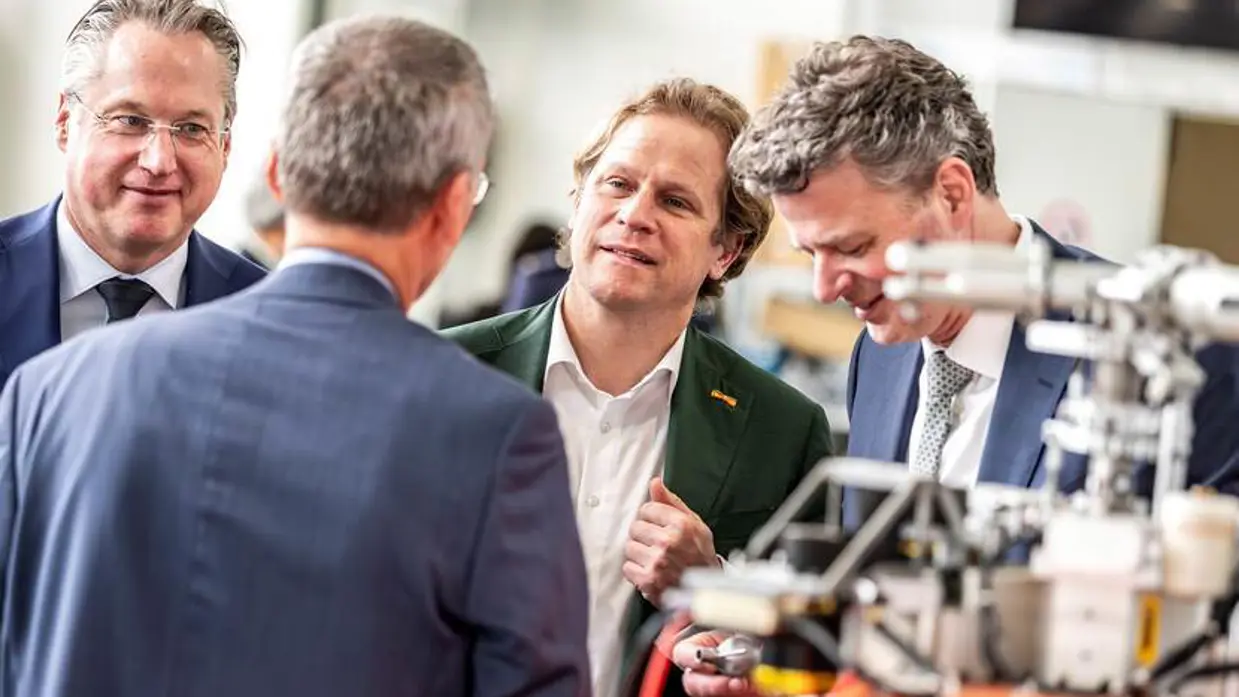 Gijs Tuinman in gesprek met 3 mannen. Op voorgrond niet te identificeren apparaat.