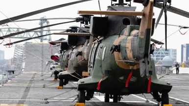 Twee oorlogsschepen liggen in een haven en op een groot schip staan helikopters opgesteld.