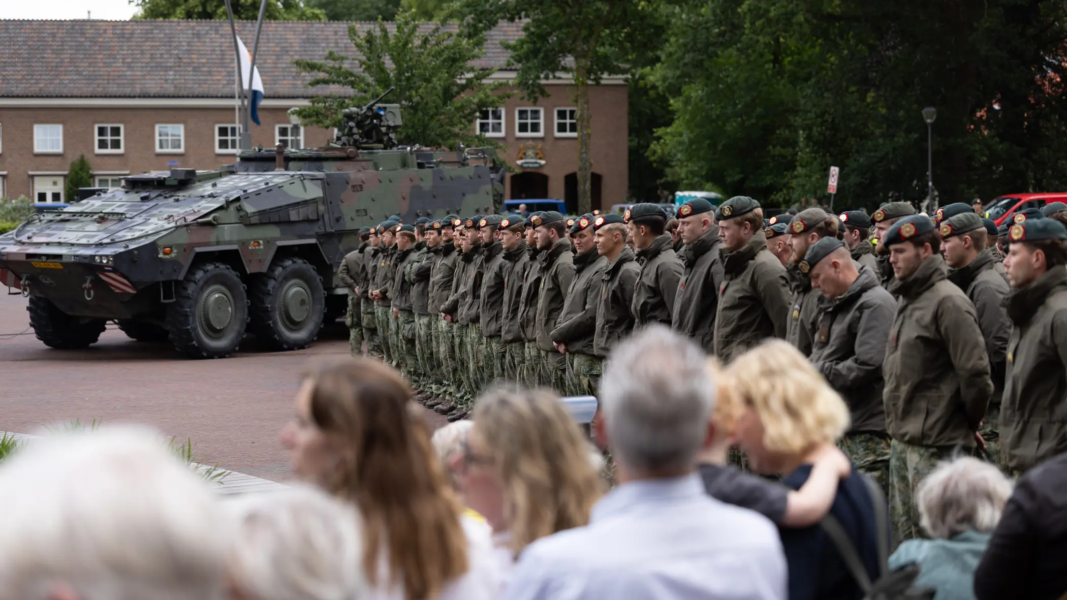 Groep militairen staat op plein met publiek aan de zijkant.