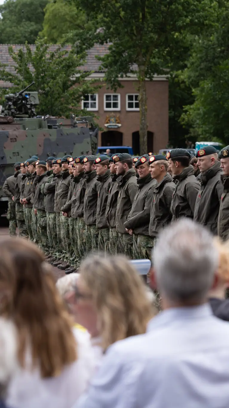 Groep militairen staat op plein met publiek aan de zijkant.