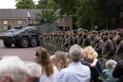 Groep militairen staat op plein met publiek aan de zijkant.