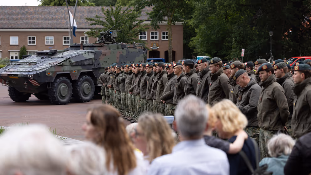 Groep militairen staat op plein met publiek aan de zijkant.