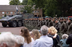 Groep militairen staat op plein met publiek aan de zijkant.