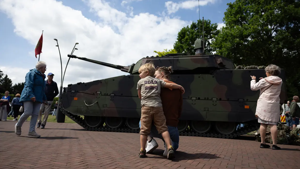 Kind speelt voor geparkeerde CV90-infanteriegevechtsvoertuig.