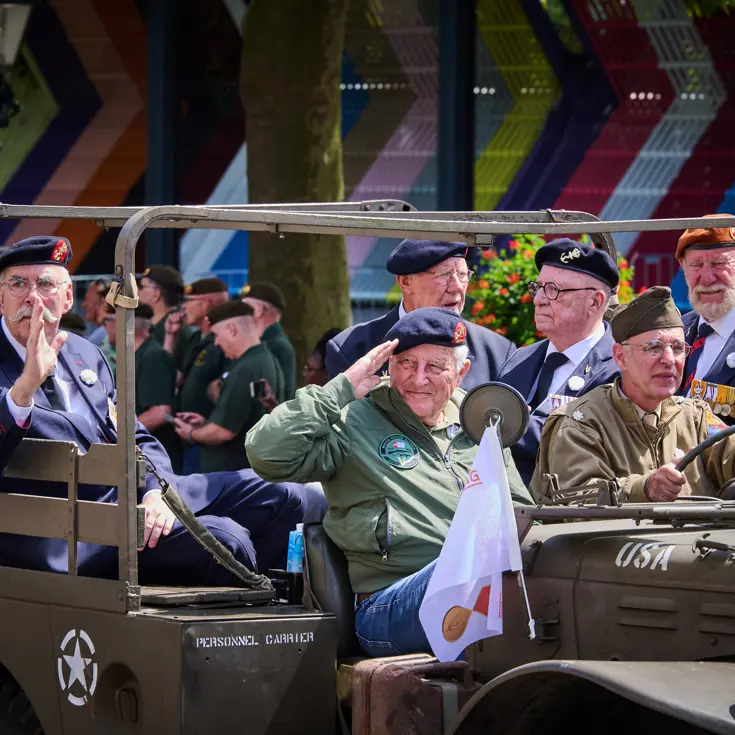 Veteranen salueren vanuit een jeep naar het publiek