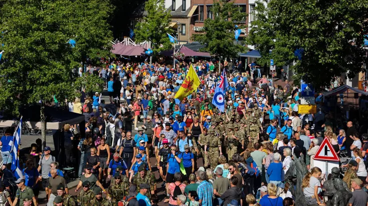Militairen en wandelaars van de Vierdaagse lopen door straat met rijen publiek die hen aanmoedigen.
