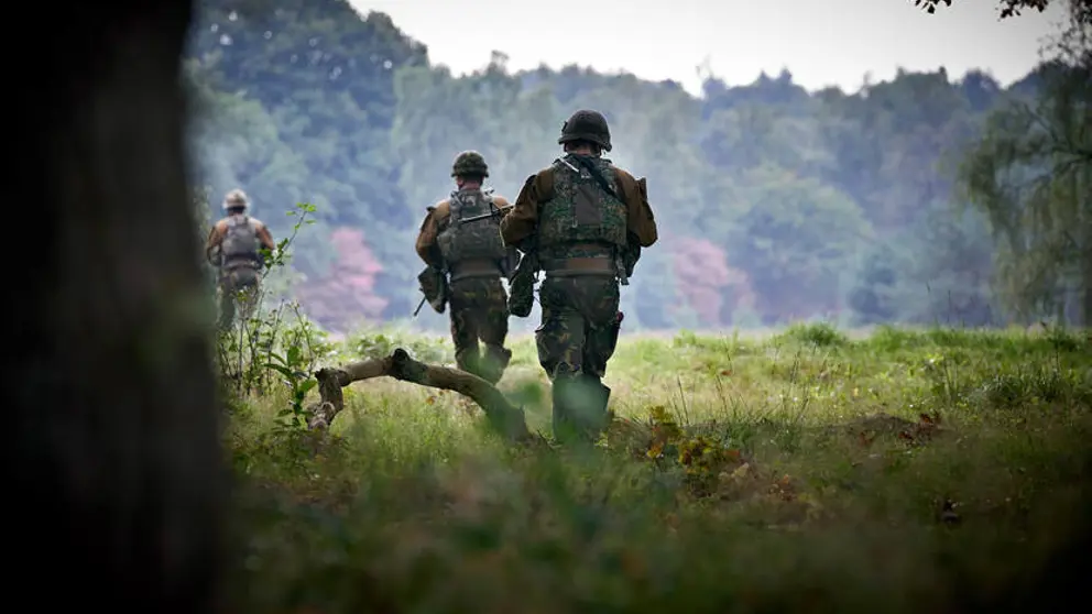 Militairen van achteren gezien lopen door een landschap.