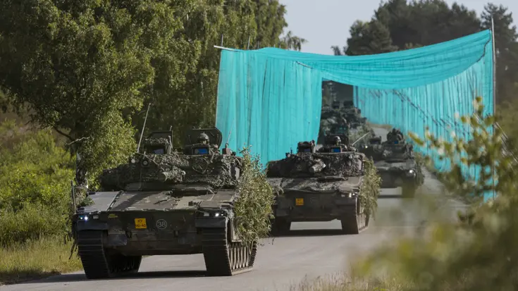 Militaire voertuigen rijden onder een antidronenet door. 