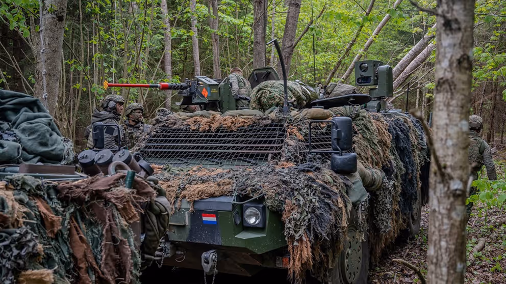 Militair voertuig voorzien van camouflage tussen de bomen.