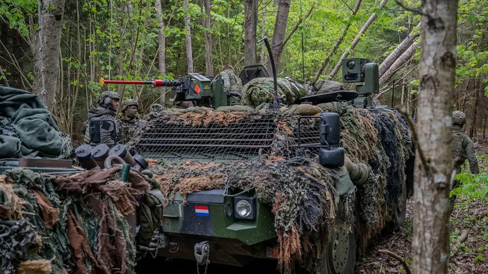 Militair voertuig voorzien van camouflage tussen de bomen.