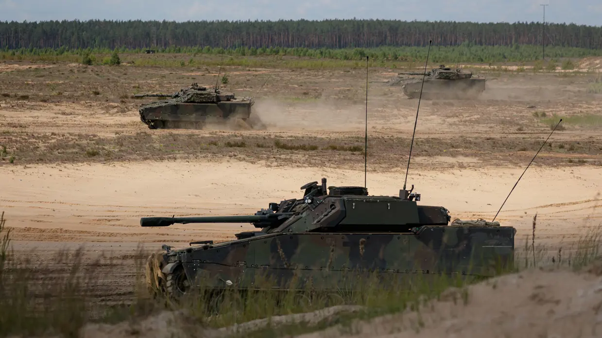Drie tanks rijden over een zandvlakte