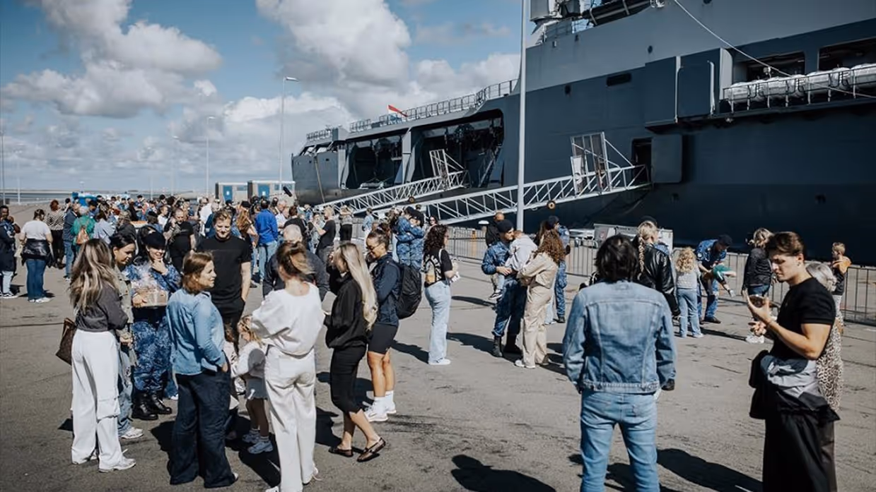 Mensen wachten op de kade voor het vertrek van een marineschip.