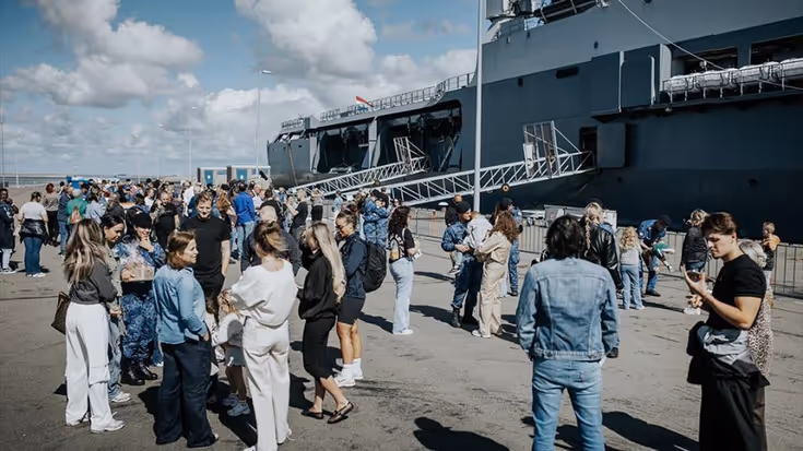 Mensen wachten op de kade voor het vertrek van een marineschip.