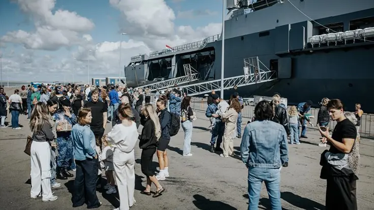 Mensen wachten op de kade voor het vertrek van een marineschip.
