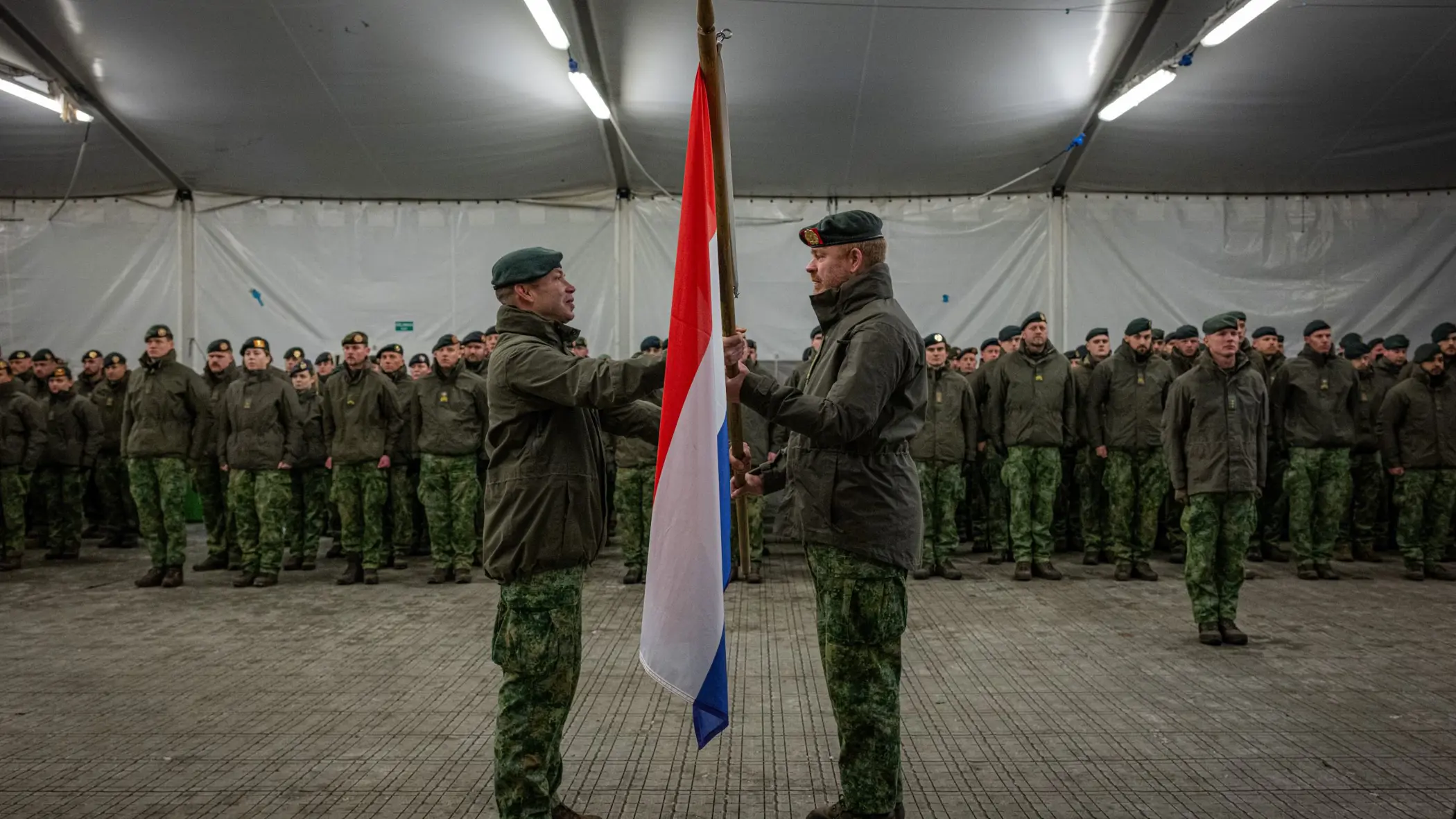 Alt-tekst: 2 militairen staan tegenover elkaar en houden Nederlandse vlag vast. 