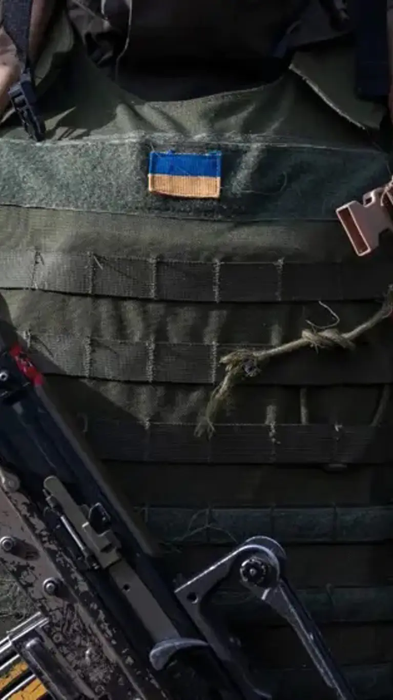 Oekraïense militair in donkere gevechtsuitrusting met een Oekraïense vlag op het kogelwerende vest en een geweer voor de borst.