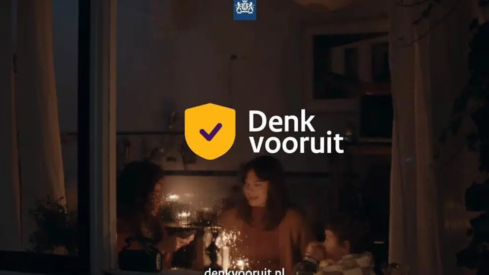 'Denk vooruit' staat op een foto genomen door een raam van 2 vrouwen en een kind die alleen kaarsjes aan hebben.
