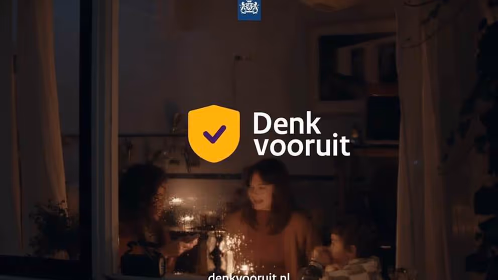 'Denk vooruit' staat op een foto genomen door een raam van 2 vrouwen en een kind die alleen kaarsjes aan hebben.