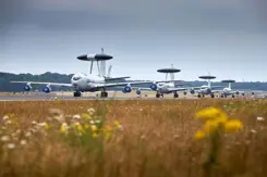 4 Awacs-toestellen op de landingsbaan met bloemetjes op de voorgrond.