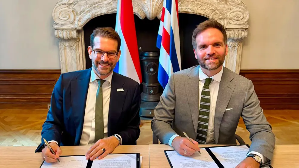 Twee mannen zitten achter een tafel en ondertekenen een formulier.