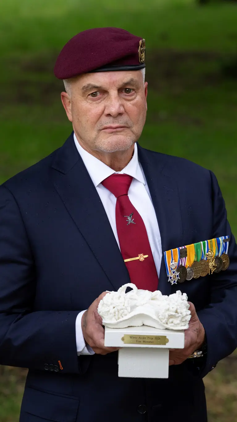 Veteraan houdt een beeldje van een witte anjer in zijn handen. 