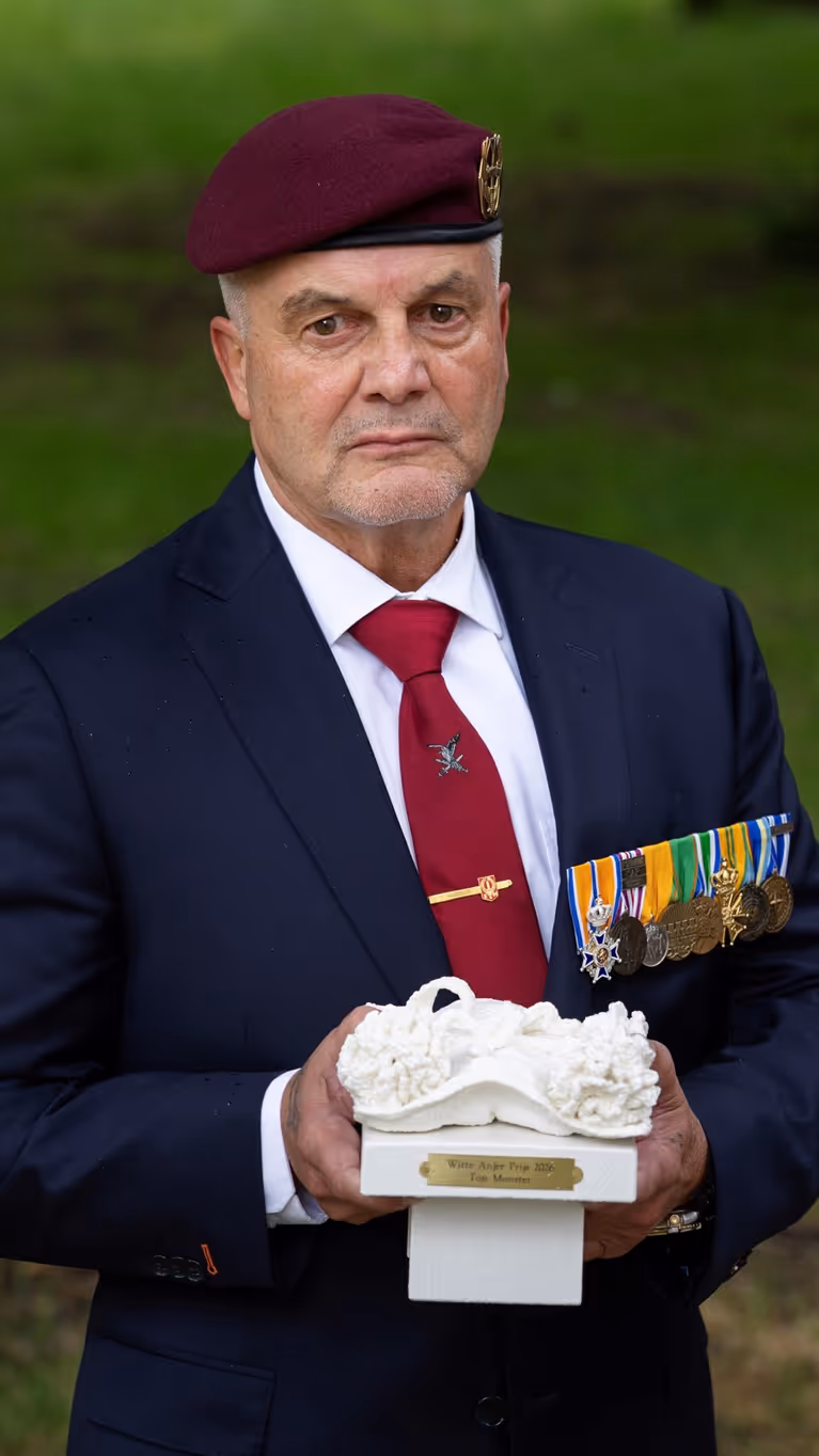 Veteraan houdt een beeldje van een witte anjer in zijn handen. 