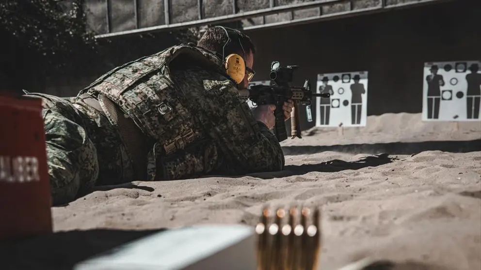 Militair ligt plat op de grond tijdens schietoefening en richt wapen op doel.