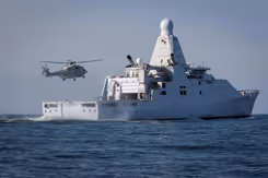 Marineschip Zr.Ms. Groningen op zee. Erboven vliegt een NH90 maritieme gevechtshelikopter.